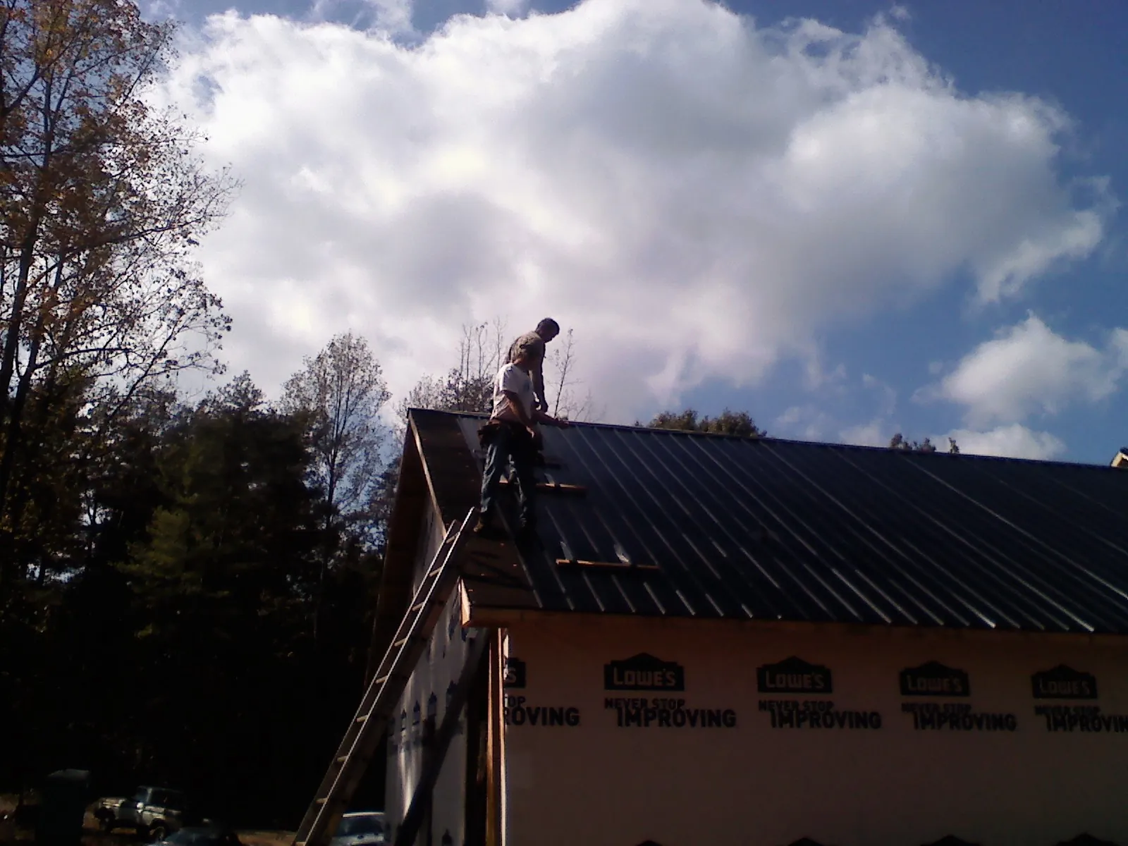 Roofer fastening dark metal panels high against a cloudy sky, from a Roof Inspection job in Summersville