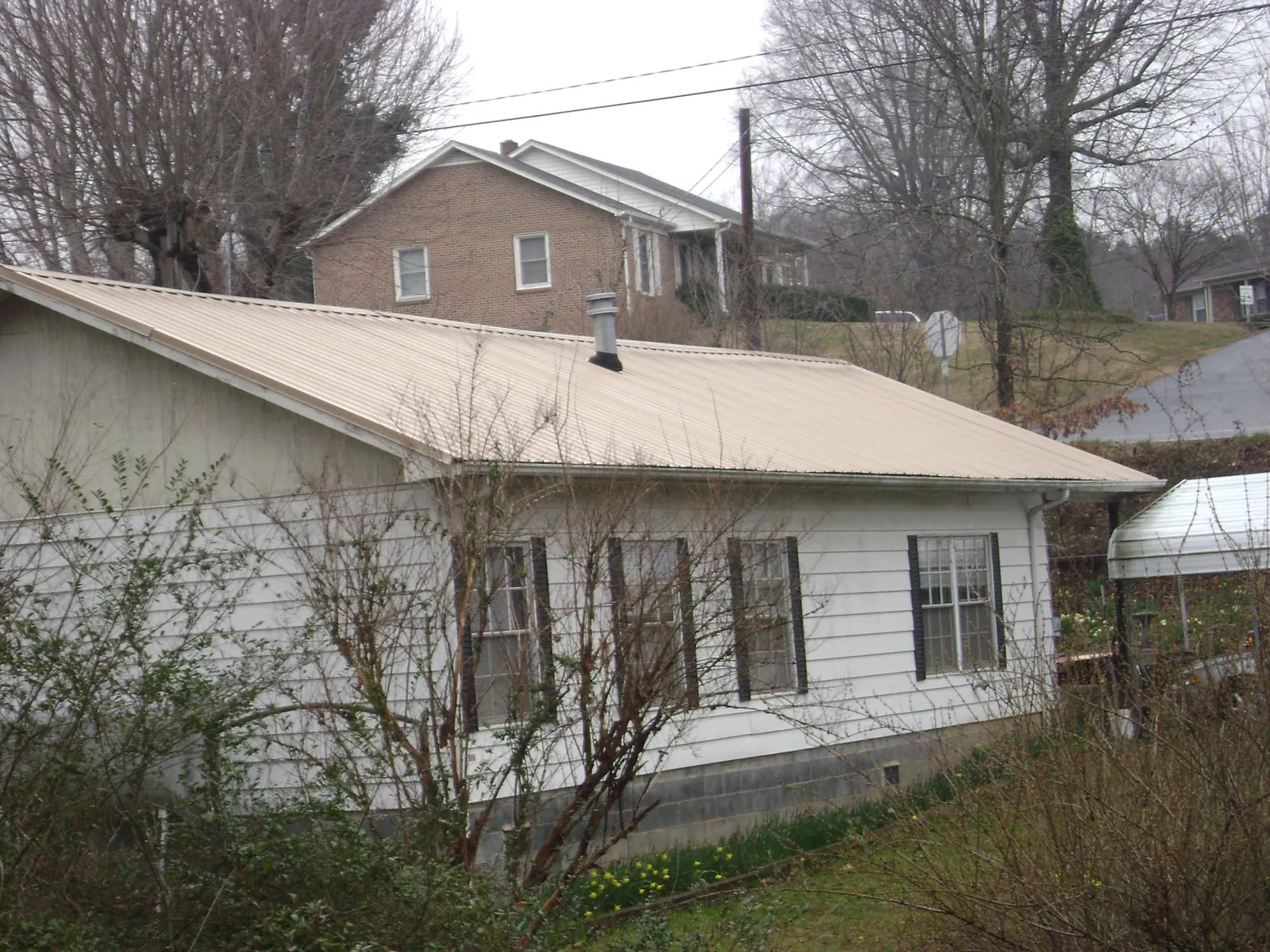 Tan metal roof on a white sided house set into a hillside — Commercial Roofing by Roofing Brothers in Summersville
